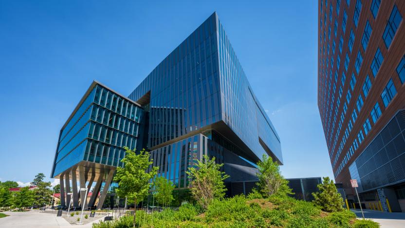 Shiny, reflective, angular, window-covered building with greenery in foreground.