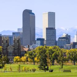Denver CO skyline with park, green trees and grass in foreground and mountains in background.