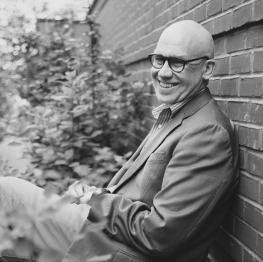 Mike Remshard sits and leans against a wall while smiling at the camera.